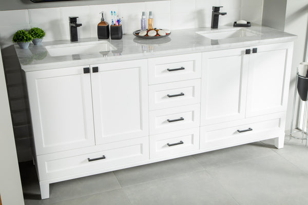 White double-sink bathroom vanity with a marble countertop, black fixtures, six drawers, and two cabinets. Toiletries, soap dispensers, and a small plant are arranged on the counter. The floor is gray tile.
