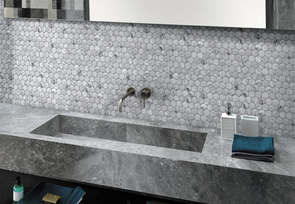 Modern bathroom sink with a rectangular stone basin, wall-mounted faucet, round marble tile backsplash, and countertop items including soap dispensers and neatly folded towels.