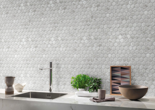 A modern kitchen counter with a round pebble-patterned white backsplash, a sink with a sleek faucet, potted herbs, a framed geometric print, and brown ceramic bowls on a marble countertop.