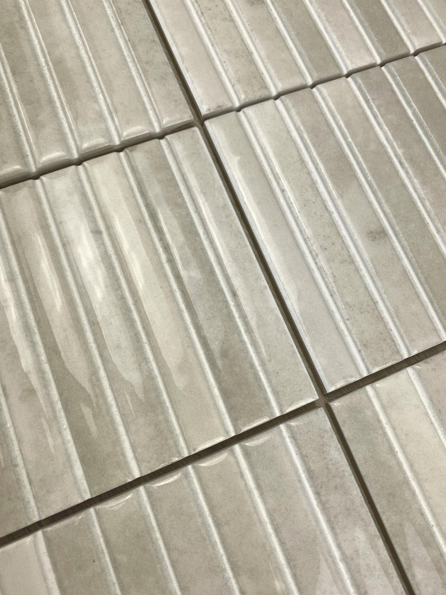 Close-up view of light gray rectangular tiles with a ribbed texture, arranged in a grid pattern. The tiles have a glossy finish and visible grout lines between them.