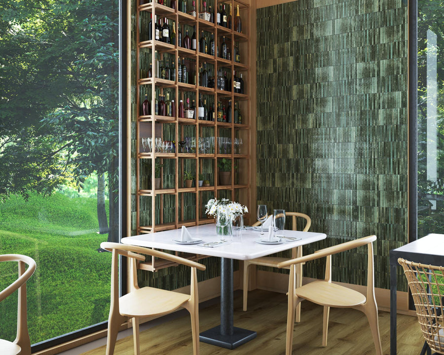 A cozy corner in a restaurant with a small marble table, wooden chairs, a wine rack filled with bottles and glasses, green textured wall, and large windows overlooking a lush, green outdoor scene.