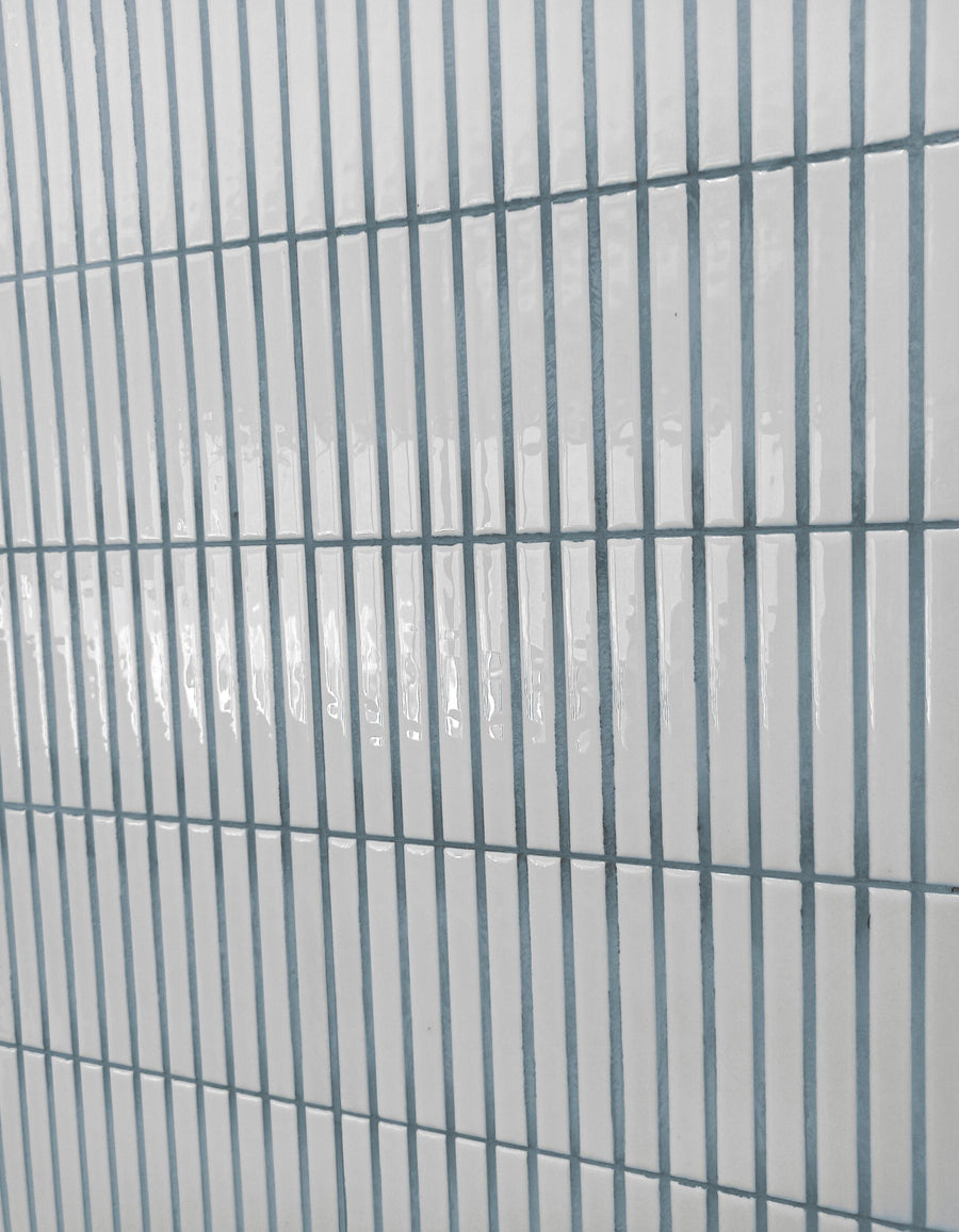 White rectangular tiles arranged in a vertical grid pattern with light gray grout lines, creating a clean and modern appearance. The tiles have a glossy finish and reflect light.