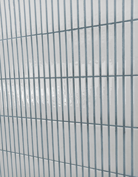 White rectangular tiles arranged in a vertical grid pattern with light gray grout lines, creating a clean and modern appearance. The tiles have a glossy finish and reflect light.
