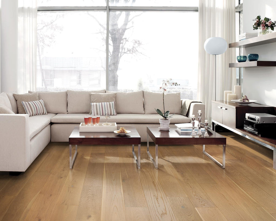 A modern living room with a large beige sectional sofa, two wooden coffee tables with chrome legs, decorative items, and floor-to-ceiling windows letting in natural light. Shelves and a record player are visible on the right.
