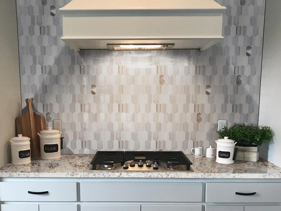 A modern kitchen stove with a marble countertop, hexagonal tile backsplash, range hood, and containers labeled “sugar,” “flour,” and “coffee.” Wooden cutting boards and a small potted plant are on the counter.