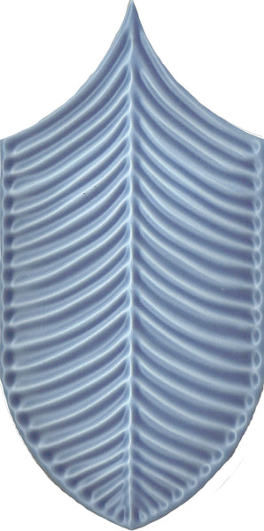 A blue, shield-shaped Plume 4x8 Ceramic Tile features a raised, symmetrical leaf vein or fishbone pattern on a white background, adding a modern and contemporary touch.