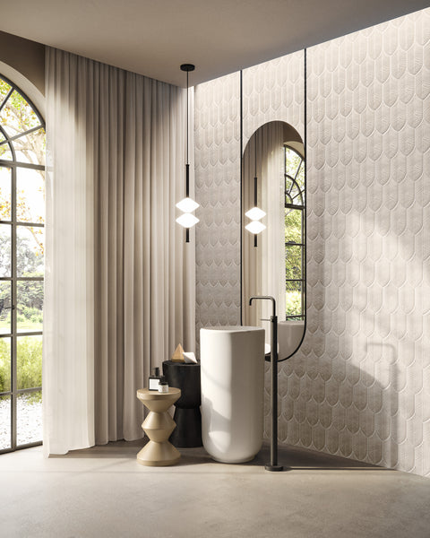 A modern bathroom with a freestanding white sink, tall oval mirror, geometric pendant lights, a small side table with decor, cream textured wall tiles, and large window with curtains overlooking greenery outside.