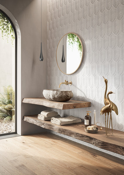 Minimalist bathroom with floating wooden shelves, a stone sink, round mirror, gold faucet, and gold crane sculptures. Rolled towels and toiletries are neatly arranged; soft light enters from an arched window with plants outside.