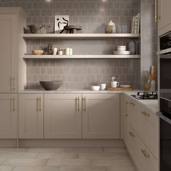 A modern kitchen with beige cabinets, brass handles, open wooden shelves displaying dishes and decor, a tiled backsplash, and a gas stovetop on a light countertop.