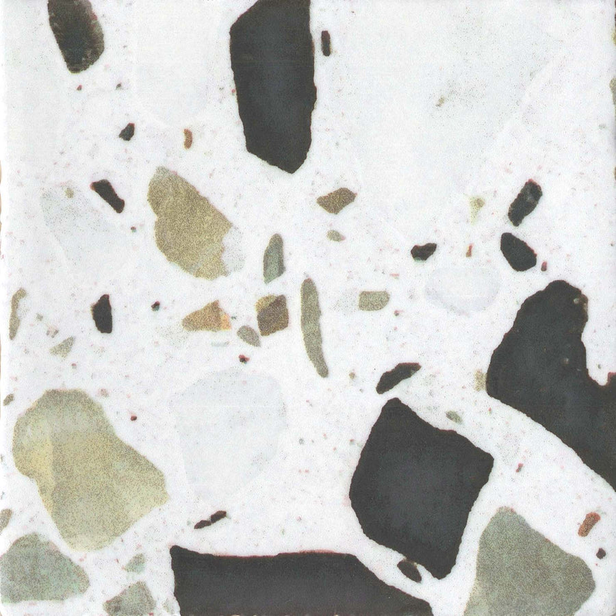 A close-up of the Fragmento 5x5 Ceramic Tile in Pop Rocks, showcasing irregular black, beige, and grey stone chips on a white background for a striking terrazzo-inspired pattern.