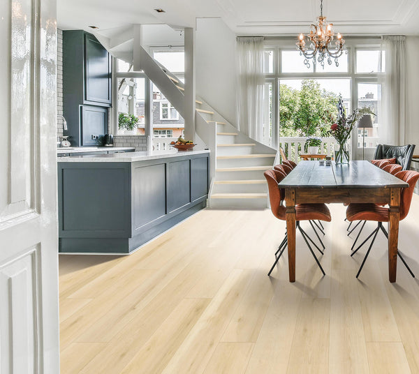 Bright, modern open-plan kitchen and dining area with light wood flooring, a dark kitchen island, wooden dining table with brown chairs, large windows, white staircase, and a chandelier. Natural light fills the space.