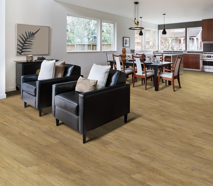Open-plan living and dining area with light wood flooring, two black armchairs with neutral cushions, a dining table set for eight, modern kitchen appliances, and large windows letting in natural light.