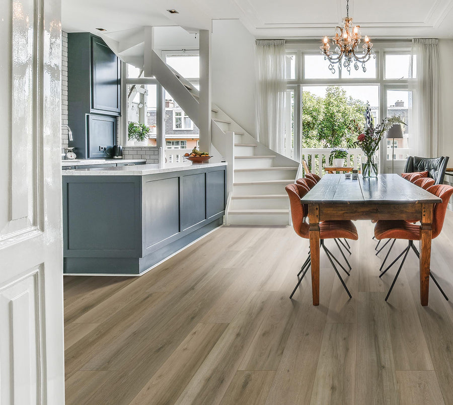 Bright, modern kitchen and dining area with light wood floors, a dark gray kitchen island, orange dining chairs around a wooden table, large windows, and a white staircase in the background.