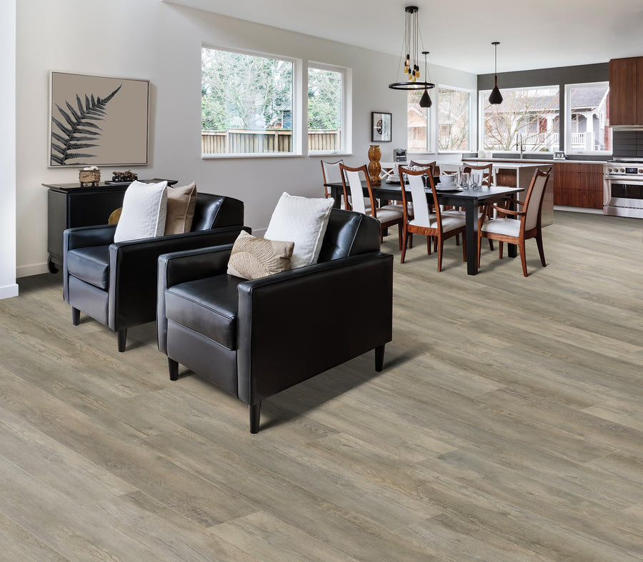 Open-plan living and dining area with wood flooring, two black armchairs with cushions, a dining table with chairs, large windows, and modern kitchen appliances in the background.