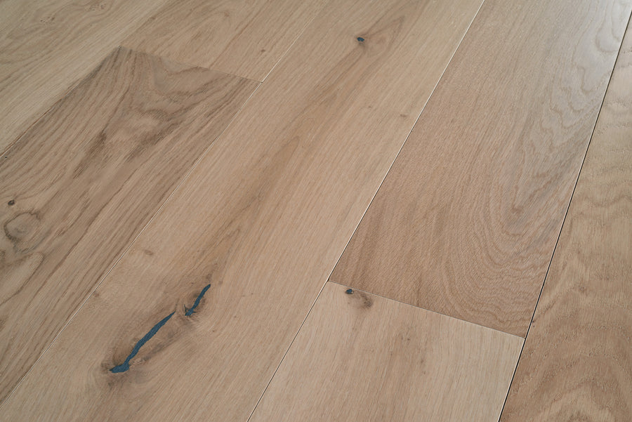Close-up view of light-colored wooden floorboards with natural wood grain patterns and a few dark knots and streaks.