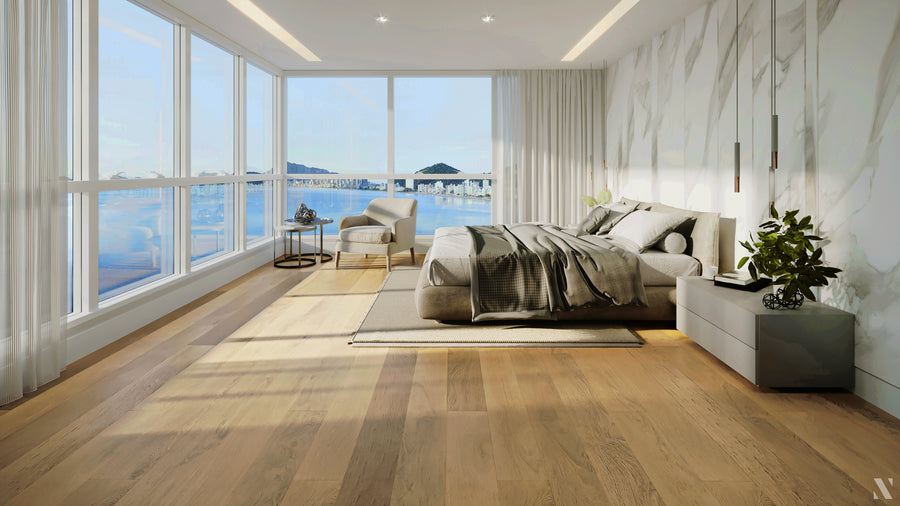 Modern bedroom with large floor-to-ceiling windows offering a scenic view of water and distant hills, featuring a gray bed, bedside tables, a chair, and light wood flooring.