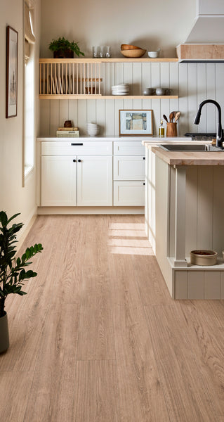 Bright, modern kitchen with white cabinets, light wood floors, open shelving, a black faucet, marble countertop island, and a green potted plant in the corner. Sunlight streams in from a window on the left.