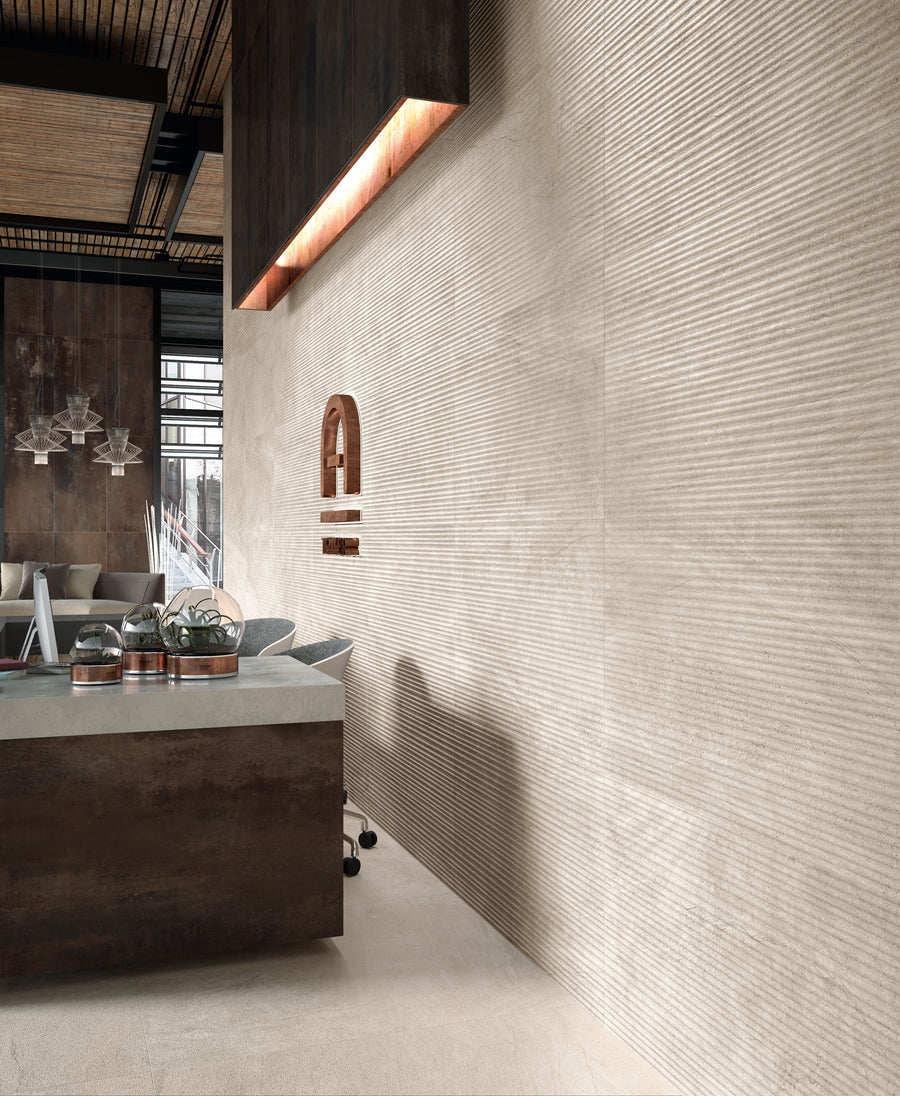Modern office interior with a textured beige wall, a dark reception desk, a curved decorative feature on the wall, and large windows letting in natural light. Industrial and minimalist design elements are visible.