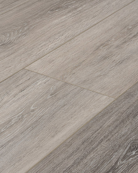 Close-up view of Moda Living 7.15" Luxury Vinyl Plank flooring, featuring light gray wood-look planks with a natural grain texture, subtle color variations, and a scratch-resistant finish.
