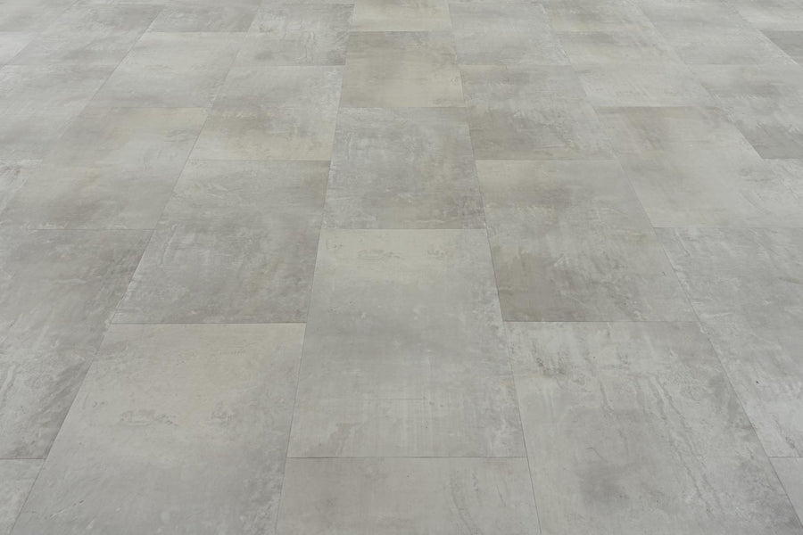 A close-up view of a floor covered with Stonescape Luxury Vinyl Plank, featuring large, rectangular gray tiles in a staggered pattern and offering durable, textured flooring with concrete-like stone aesthetics.