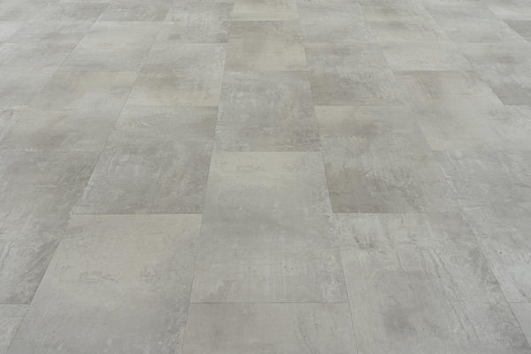 A close-up view of a floor covered with Stonescape Luxury Vinyl Plank, featuring large, rectangular gray tiles in a staggered pattern and offering durable, textured flooring with concrete-like stone aesthetics.