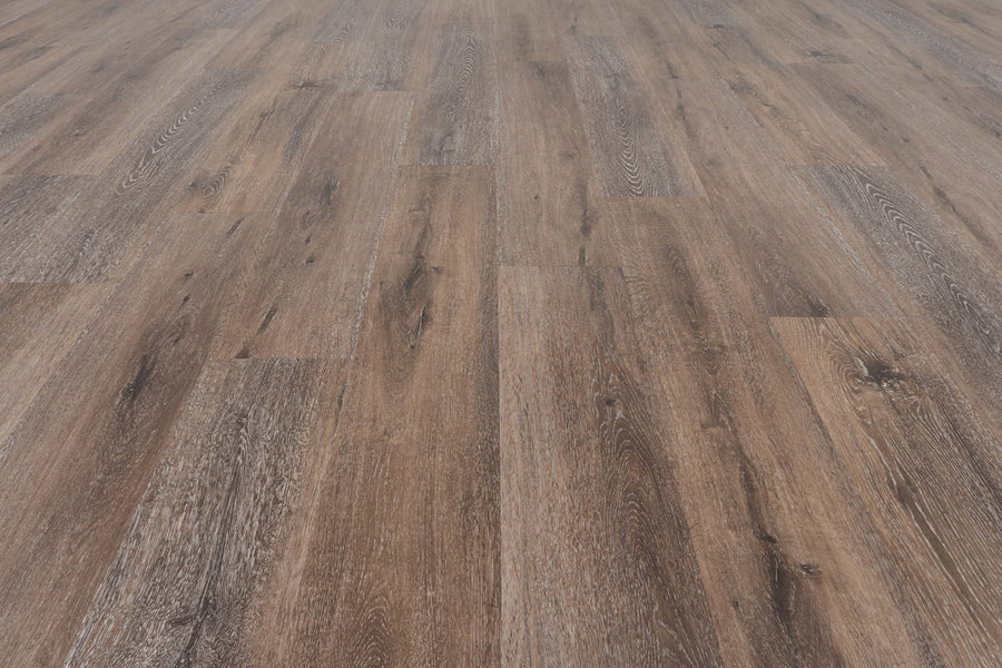 Close-up view of Uptown Chic 7.15" Luxury Vinyl Plank flooring with wide planks in a natural brown shade and distinct wood grain, creating a rustic, warm look that extends into the distance.