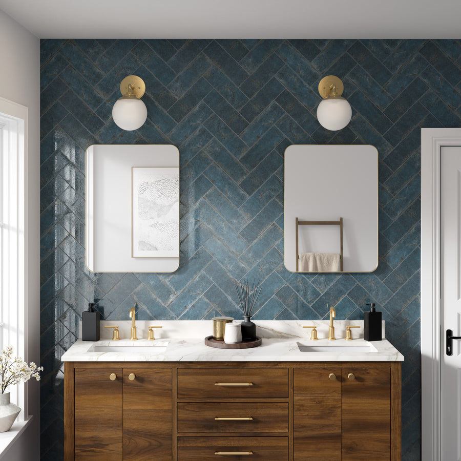 Modern bathroom with a wooden double-sink vanity, white marble countertop, gold fixtures, and blue herringbone-tiled wall. Two rectangular mirrors and round wall lights are above each sink, and a towel rack is on the right wall.