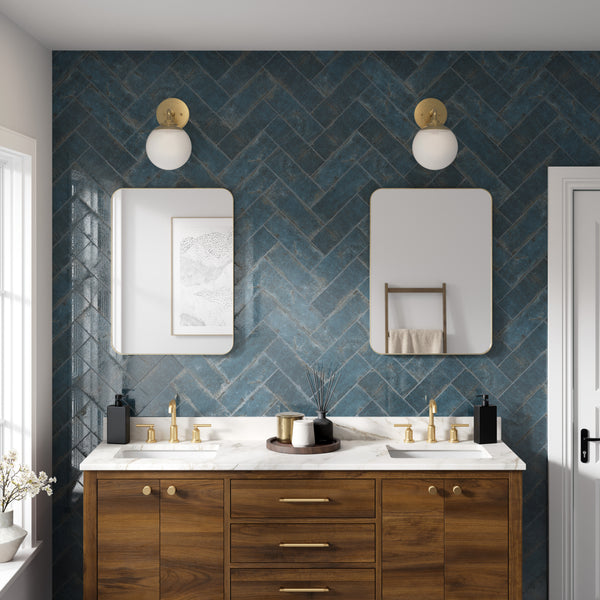 Modern bathroom with a wooden double-sink vanity, white marble countertop, gold fixtures, and blue herringbone-tiled wall. Two rectangular mirrors and round wall lights are above each sink, and a towel rack is on the right wall.