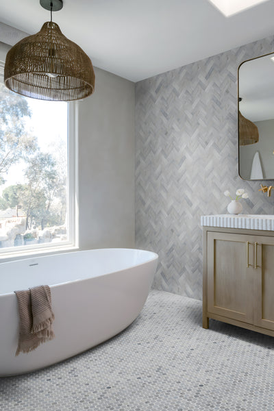 Modern bathroom with a freestanding white tub, taupe towel, large window, rattan pendant light, wood vanity with striped countertop, and a Blue Horizon 1