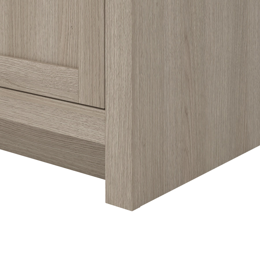 Close-up view of the bottom corner of a light wood cabinet, showing its textured grain and smooth finish. The image focuses on the joinery and surface detail.