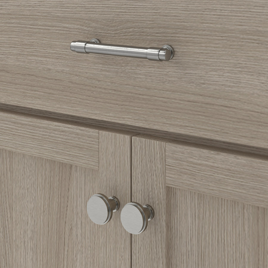 Close-up of a light wood cabinet with a horizontal metal handle on a drawer above and two round metal knobs on double doors below.