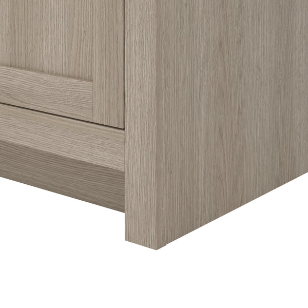 Close-up of the bottom corner of a light wood cabinet, showing the texture and grain of the material. The image focuses on the side and front panels against a white background.