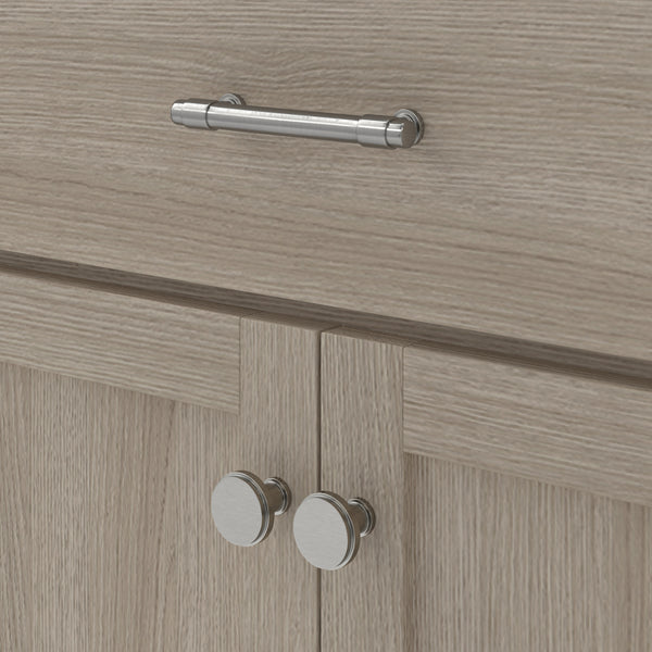 Close-up of light wood kitchen cabinets with silver round knobs on the lower doors and a silver horizontal bar handle on the upper drawer. The wood has a subtle grain texture.