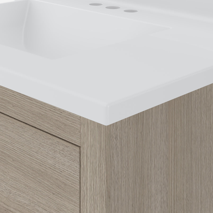 Close-up of a bathroom vanity with a white countertop and integrated sink, featuring a light wood cabinet with a drawer and three faucet holes visible on the countertop.