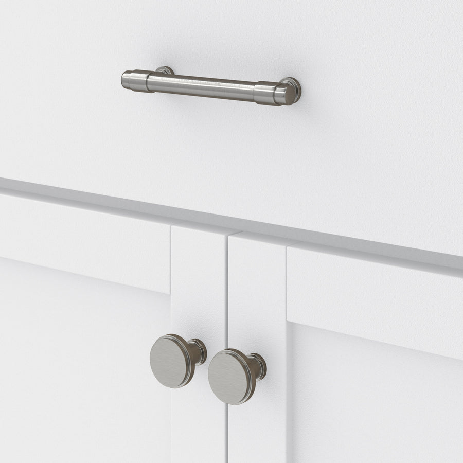 Close-up of white cabinet doors with two round silver knobs, and a drawer above featuring a horizontal silver handle. The surface is smooth and clean.