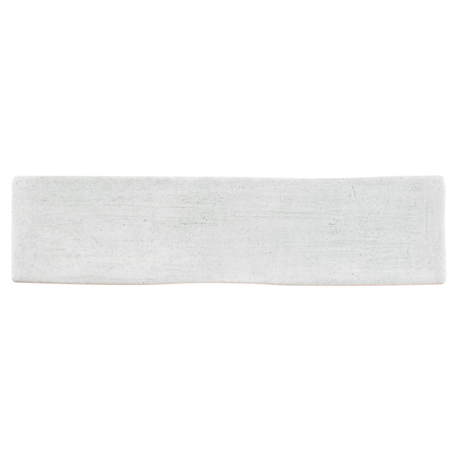 The Rhythmique 3" x 12" ceramic subway tile in grey features a rectangular shape, slightly uneven surface, and rough edges, making it perfect for contemporary interiors. Shown here against a plain white background.