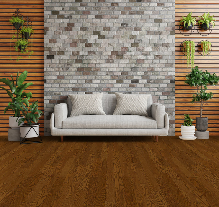 A modern living room with a light gray sofa, patterned cushions, a brick accent wall, wood paneling, and various potted and hanging green plants arranged around the space.