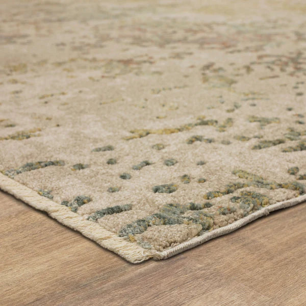 Close-up view of a beige and light green patterned area rug with a textured surface, shown on a wooden floor. The rugs edge is slightly raised, revealing its thickness and woven border.