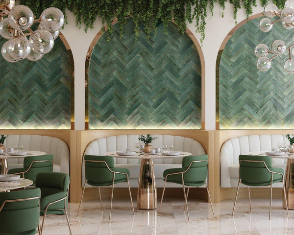 A stylish restaurant interior with green chevron wall panels, gold accents, round tables, green chairs, white cushioned booths, hanging glass globe lights, and greenery on top of arched wall niches.