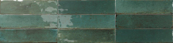 Two rows of Relic 2.7 x 11 Porcelain Tile in green, with a glossy finish and shade variation. Subtle reflections and dark grout lines highlight the handcrafted, rustic appeal.