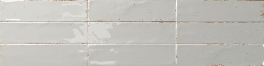 The Relic 2.7 x 11 Porcelain Tile features glossy off-white, rectangular tiles with a slightly uneven surface, subtle brownish grout lines, and shade variation for a rustic, handcrafted look when installed in a staggered pattern.