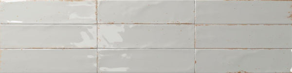 The Relic 2.7 x 11 Porcelain Tile features glossy off-white, rectangular tiles with a slightly uneven surface, subtle brownish grout lines, and shade variation for a rustic, handcrafted look when installed in a staggered pattern.