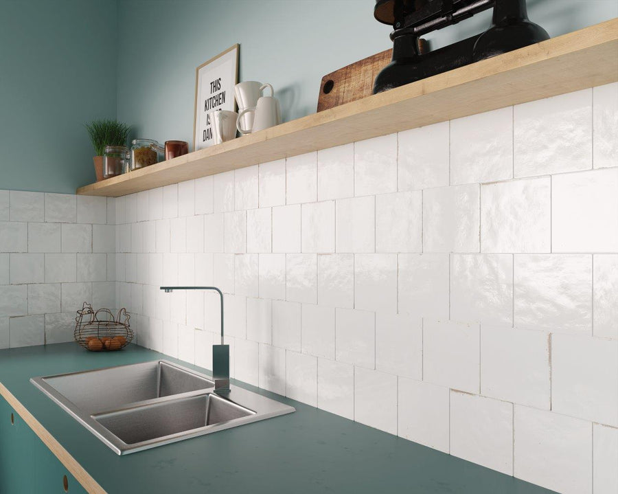 Modern kitchen with a teal countertop, stainless steel sink, white square tile backsplash, and a wooden shelf holding jars, cups, and decor items against a light blue wall.