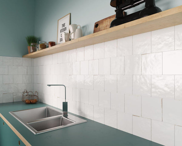 Modern kitchen with a teal countertop, stainless steel sink, white square tile backsplash, and a wooden shelf holding jars, cups, and decor items against a light blue wall.