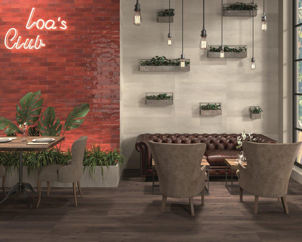 A cozy cafe interior with a brown leather sofa, beige armchairs, a round table, hanging light bulbs, wall-mounted planters, and a red brick wall with a neon sign reading Loas Club.
