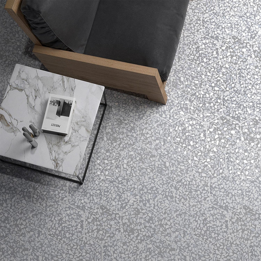 A gray terrazzo hexagon-patterned floor next to a light wood sofa with dark gray cushions. A marble coffee table holds a magazine and a decorative object.