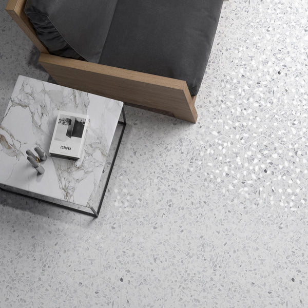 A modern living room scene with a light terrazzo floor, a marble-top coffee table holding a magazine and decorative object, and part of a gray-cushioned wooden sofa.