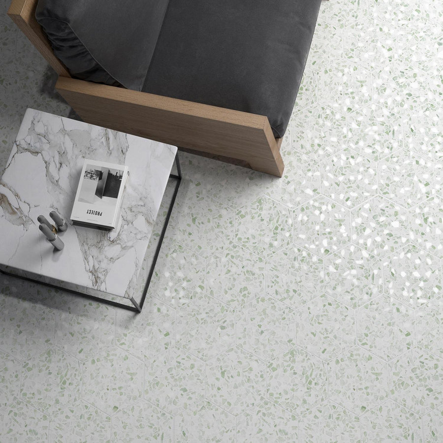 A top-down view of a gray cushioned wooden sofa next to a white marble coffee table with a book and headphones, set on a light terrazzo floor with subtle green flecks.