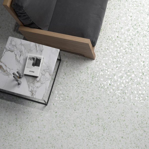 A top-down view of a gray cushioned wooden sofa next to a white marble coffee table with a book and headphones, set on a light terrazzo floor with subtle green flecks.