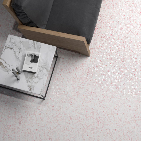 A marble coffee table with a magazine and headphones sits next to a grey sofa on a floor with light pink and white terrazzo tiles.